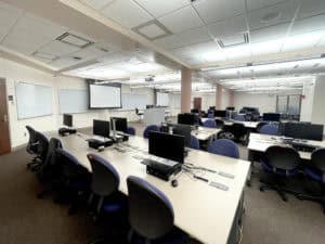 Image showing classroom space with two retractable screens, 4 white boards, instructor podium, and seats with computers for 25 students
