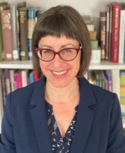 Woman with bob haircut and glasses stands in front of a bookcase and smiles at the camera