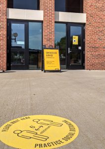 View of the south entrance to the Main Library with a spot on teh ground about 20 feet outside the entrance designated "Please wait here"