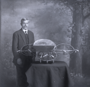 Photograph of Frank Brinton standing next to one of his airship models