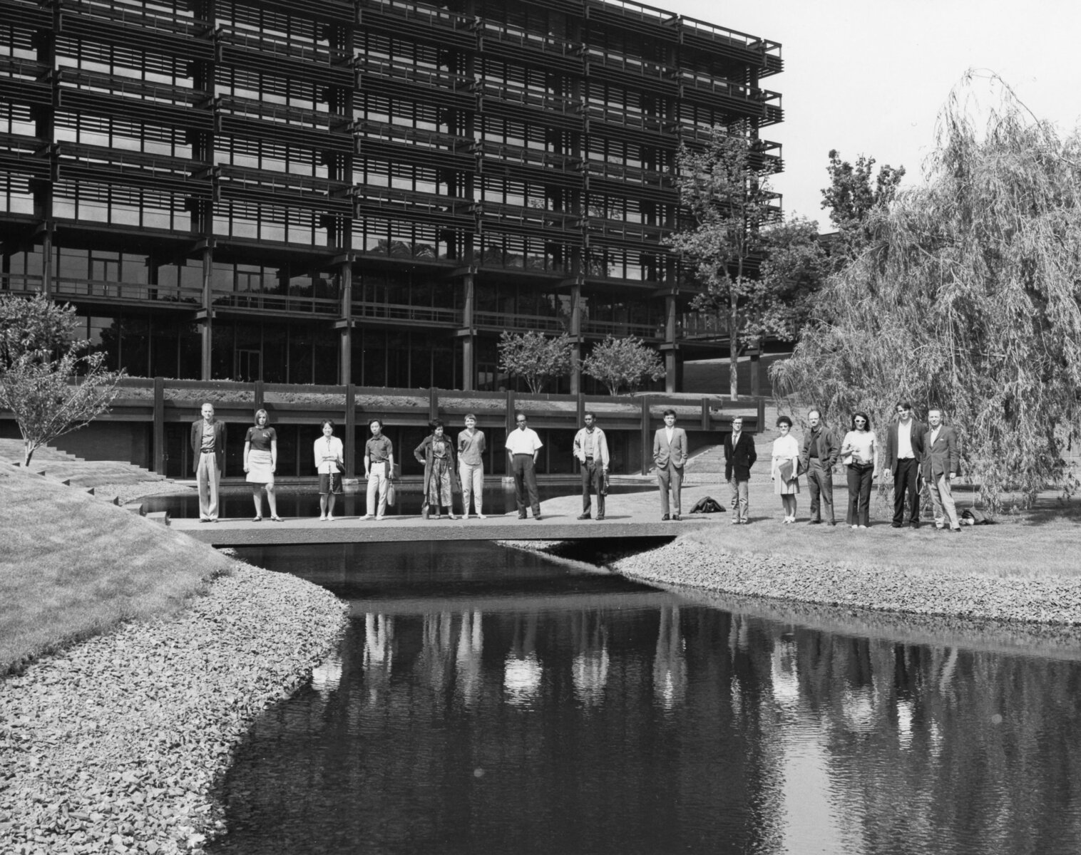 Several international writers stand side by side, spanning across a small bridge that stretches over a ravine outside the massive John Deere headquarters in Moline, Illinois.
