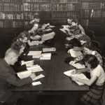 Black and white photo of 13 student studying at a long table.