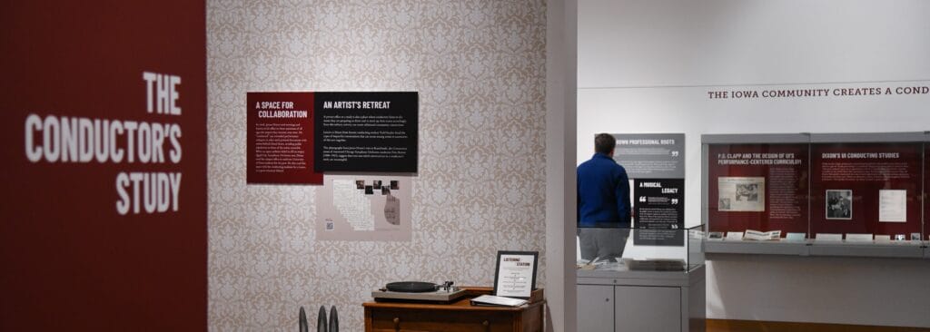 A person stands in a gallery, which contains many display cases and a specially-created conductor's study with a record player and ornate wallpaper.