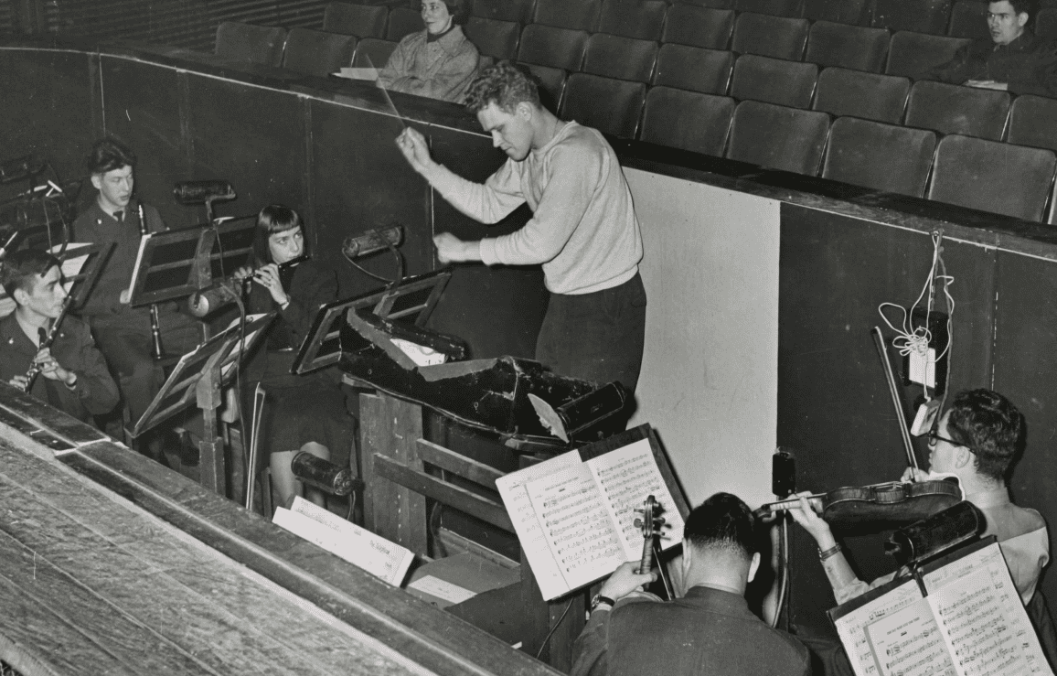 Jamex Dixon conducts a small orchestra pit in rehearsal for a theatre show.