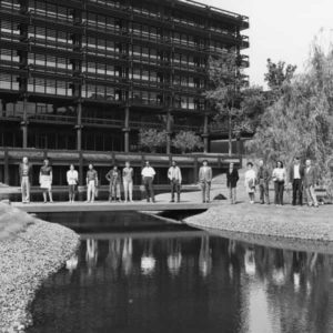 Several international writers stand side by side, spanning across a small bridge that stretches over a ravine outside the massive John Deere headquarters in Moline, Illinois.
